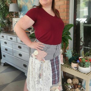 May include: A woman wearing a burgundy v-neck t-shirt and a patchwork skirt made from denim and various fabrics. The skirt features lace, striped, and plaid patterns. She is wearing brown sandals.