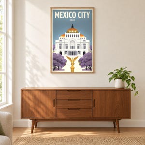 Può includere: Un poster da viaggio incorniciato intitolato MEXICO CITY CDMX che raffigura un edificio bianco con una cupola dorata, una statua alata dorata in primo piano e alberi viola su un cielo azzurro, esposto in una cornice di legno.