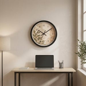 May include: A round wall clock with a black frame and a beige face featuring a botanical illustration of green leaves on the left side. The clock has black hour, minute, and second hands, and black numerals from one to twelve printed on the face.