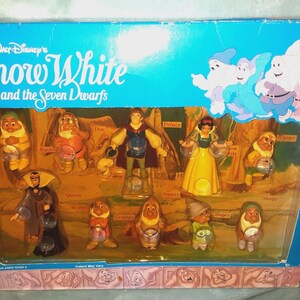 Op de afbeelding: Een Walt Disney's Snow White and the Seven Dwarfs doosset met plastic figuren van Sneeuwwitje, de Prins, de Koningin en de zeven dwergen. Elk personage wordt getoond in een doos met een venster en een kartonnen achtergrond met bosmotief.