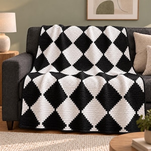 May include: A rectangular crochet blanket featuring a repeating black and white diamond pattern. The textile is constructed with a visible yarn stitch texture, creating a high-contrast geometric design that covers the entire surface of the throw.
