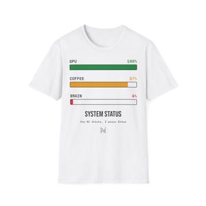Può includere: Una t-shirt bianca a maniche corte con un grafico di tre barre di avanzamento etichettate GPU al 100%, COFFEE all'87% e BRAIN al 4%. Sotto le barre, il testo recita SYSTEM STATUS, the AI thinks, I press Enter, e un piccolo logo.