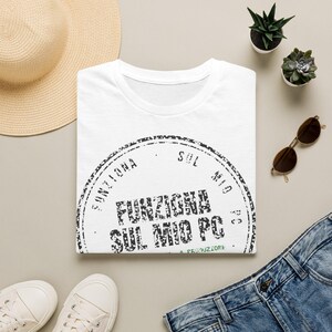 Può includere: Una t-shirt bianca a maniche corte con una grafica a timbro circolare nera con il testo "FUNZIONA SUL MIO PC" stampato al centro e ripetuto lungo il bordo curvo, presentata in una composizione piatta.