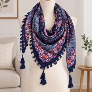 Pode incluir: Um lenço triangular em azul-marinho profundo com um padrão floral e geométrico vibrante em tons de rosa, vermelho e branco. As bordas do lenço são finalizadas com pequenas borlas azul-marinho a condizer que pendem ao longo do perímetro.