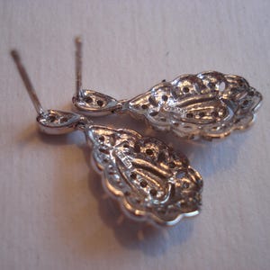 May include: A pair of silver dangle earrings with intricate filigree designs. The earrings are teardrop shaped and have a delicate, feminine look.