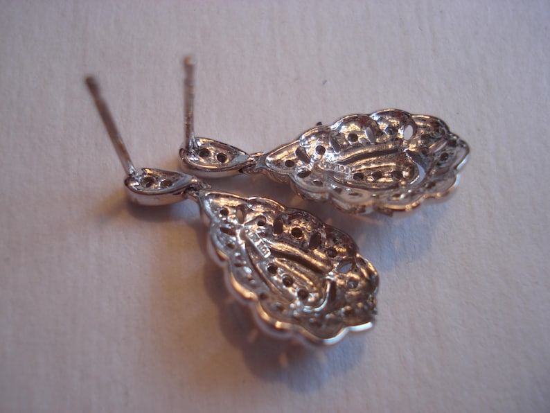 May include: A pair of silver dangle earrings with intricate filigree designs. The earrings are teardrop shaped and have a delicate, feminine look.