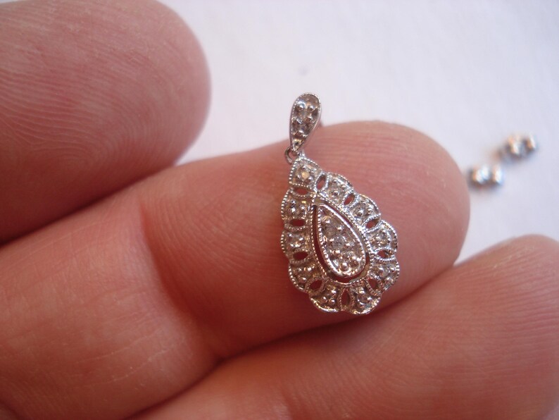 May include: A silver pendant with a teardrop-shaped design, featuring a cluster of small diamonds in the center.