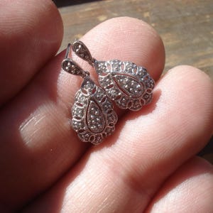 May include: A pair of silver teardrop earrings with a delicate filigree design and small clear stones.