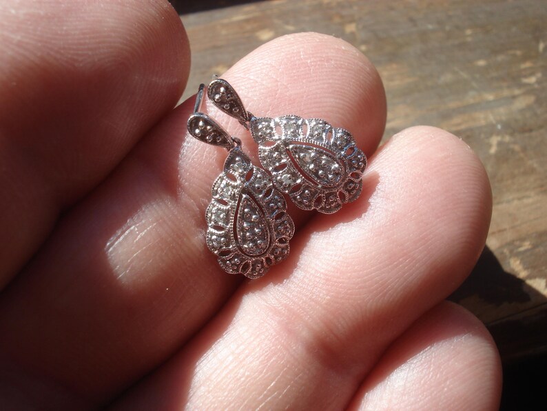 May include: A pair of silver teardrop earrings with a delicate filigree design and small clear stones.