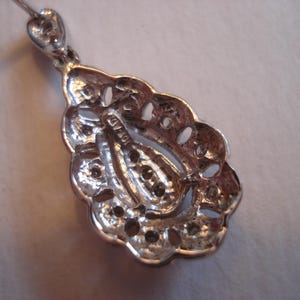May include: Silver teardrop pendant with intricate filigree design and a small, clear stone in the center. The back of the pendant has a small, engraved mark.