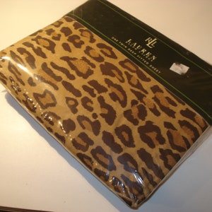 May include: A brown and tan fitted sheet with a leopard print pattern. The sheet is packaged in plastic and has a label that reads "Lauren Ralph Lauren One Twin Deep Fitted Sheet".