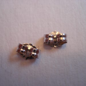 May include: Two silver earring backs, each with a small, round, textured surface and a metal loop.