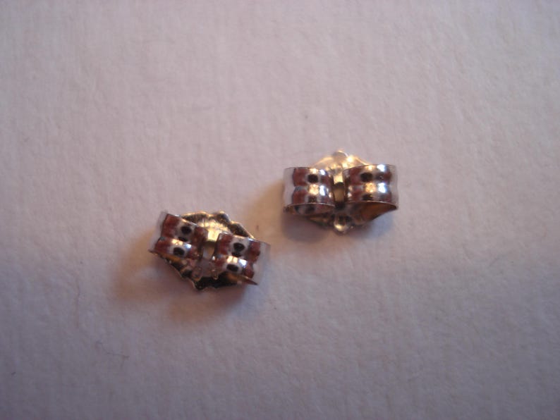 May include: Two silver earring backs, each with a small, round, textured surface and a metal loop.