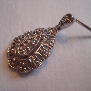 May include: Silver dangle earring with a teardrop-shaped design featuring intricate filigree work and small clear stones.
