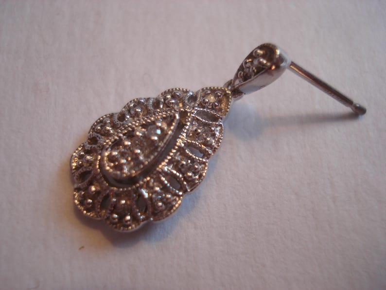 May include: Silver dangle earring with a teardrop-shaped design featuring intricate filigree work and small clear stones.