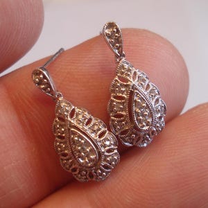 May include: A pair of silver teardrop earrings with a delicate filigree design and small clear stones.