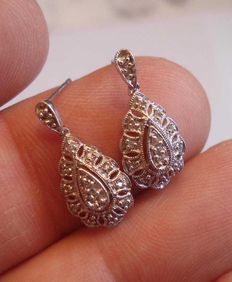 May include: A pair of silver teardrop earrings with a delicate filigree design and small clear stones.
