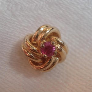 May include: A gold knot-shaped earring with a pink gemstone in the center.