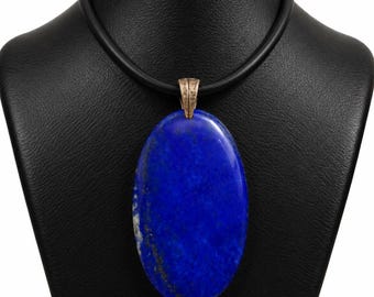 Könnte beinhalten: Ein großer, glatter, ovaler Lapis-Lazuli-Anhänger in tiefem Blau mit subtilen goldfarbenen Sprenkeln. Der Stein wird von einer strukturierten, metallisch wirkenden Öse gehalten und hängt an einer schlichten, glatten schwarzen Kautschukkette.