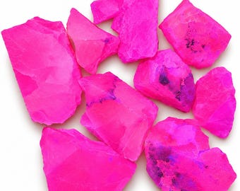 Könnte beinhalten: Eine Ansammlung von rohen, unregelmäßig geformten Steinen in einem leuchtenden Neon-Pink. Die Steine weisen scharfe, kantige Formen und texturierte Oberflächen auf, wobei einige Stücke kleine, dunkelviolette oder schwarze Einschlüsse zeigen.