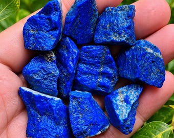 Könnte beinhalten: Eine Ansammlung von rohen Lapislazuli-Steinen mit einer tiefen, leuchtenden blauen Farbe und sichtbaren goldenen Pyrit-Einschlüssen auf den rauen, strukturierten Oberflächen jedes einzelnen Stücks, die zusammen gruppiert sind.
