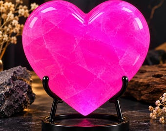 Könnte beinhalten: Eine polierte, leuchtend pinkfarbene herzförmige Steinskulptur auf einem schwarzen Metallständer. Der Stein hat eine glatte, glänzende Oberfläche mit sichtbaren inneren kristallinen Strukturen und Lichtreflexen.