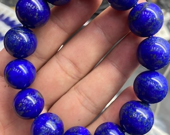 Könnte beinhalten: Ein Armband bestehend aus vierzehn polierten, kugelförmigen Lapislazuli-Perlen. Jede Perle weist eine tiefe, leuchtend blaue Farbe mit natürlichen goldfarbenen Pyriteinschlüssen auf, die über die glatten, abgerundeten Oberflächen verteilt sind.