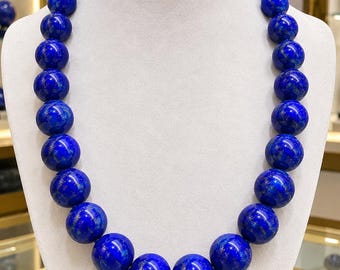 Könnte beinhalten: Eine Halskette bestehend aus großen, kugelförmigen Lapislazuli-Perlen in einem tiefen Königsblau mit natürlichen goldfarbenen Pyrit-Einschlüssen. Die Perlen sind gleichmäßig groß und zu einem durchgehenden Strang aufgereiht.