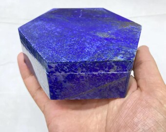 Könnte beinhalten: Eine sechseckige Schatulle aus tiefblauem Lapislazuli-Stein mit natürlichen goldfarbenen Pyriteinschlüssen auf der gesamten Oberfläche. Der Deckel schließt bündig mit dem Unterteil ab und bildet eine glatte, geometrische Form.
