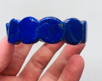 Könnte beinhalten: Ein Armband aus mehreren tiefblauen Lapis-Lazuli-Segmenten. Jedes Segment ist zu einer glatten, abgerundeten, sechseckigen Form poliert, wodurch ein durchgehendes Gliederkettendesign mit sichtbaren natürlichen goldfarbenen Pyrit-Einschlüssen entsteht.