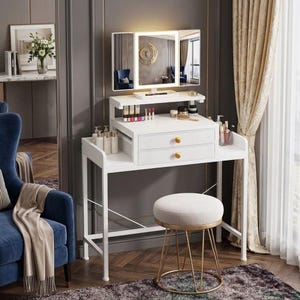 May include: A white vanity desk with two drawers featuring gold knobs, a tri-fold mirror with integrated LED lighting, and a matching round stool with a beige upholstered seat and a gold metal base, holding various cosmetics and bottles.