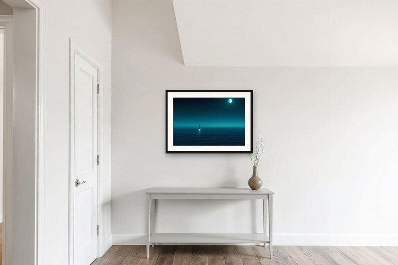 May include: A framed horizontal wall art print featuring a dark teal and blue landscape with a solitary figure standing on a calm, reflective surface under a glowing moon. The artwork is enclosed in a simple black frame and displayed on a white wall.