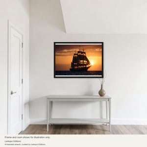 Könnte beinhalten: Ein gerahmter Wandkunstdruck mit der Silhouette eines Großseglers auf dem Ozean bei Sonnenuntergang. Das Bild zeigt den dunklen Umriss des Schiffes vor einem leuchtend orangefarbenen und gelben Himmel mit der Sonne nahe dem Horizont.