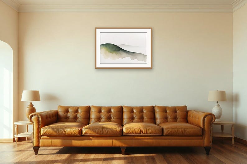 May include: A framed landscape print featuring a watercolour painting of rolling hills in shades of dark green and muted brown, set against a white background. The artwork is enclosed in a simple, light-toned wooden frame with a white mat border.