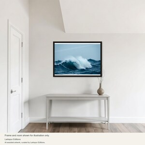 Könnte beinhalten: Ein gerahmter horizontaler Wandkunstdruck, der eine große, brechende Meereswelle mit weißem Gischt vor einem tiefblauen Meer und einem blassen, bewölkten Himmel zeigt. Das Kunstwerk befindet sich in einem dünnen schwarzen Rahmen an einer weißen Wand.