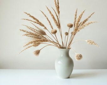 May include: A smooth, light grey ceramic vase with a narrow neck and rounded body, containing an arrangement of dried beige wheat stalks, grasses, and round seed heads that fan out in various directions, creating a natural, textured display.
