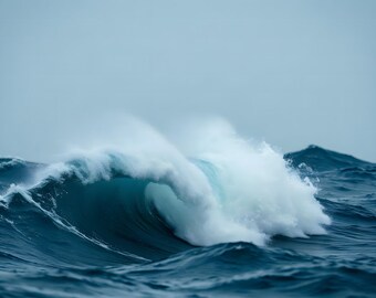 May include: A large, powerful ocean wave cresting in deep blue water. The wave features a translucent turquoise center and a thick, white foamy spray breaking at the top, set against a muted, overcast sky and a dark, turbulent sea surface.