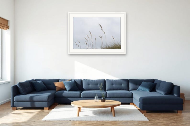 May include: A framed landscape photograph featuring tall, thin blades of beach grass swaying against a pale, overcast sky. The artwork is presented in a clean white frame, showcasing a minimalist nature scene with muted tones and soft lighting.
