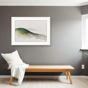 May include: A framed landscape wall art print featuring a watercolour painting of rolling hills in shades of dark green and muted beige against a light background, displayed in a white frame with a clean, simple border design.