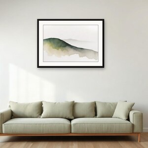 May include: A framed horizontal wall art print featuring a watercolour landscape painting of a single rolling hill in shades of muted green and beige against a white background, displayed in a simple black frame with a white mat border.