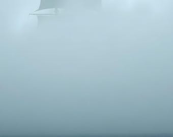 May include: A tall ship with dark sails emerges from a thick, dense layer of gray fog above a dark blue ocean. The masts and rigging are partially visible through the mist, while the hull remains obscured by the heavy atmospheric conditions.
