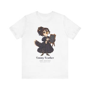May include: A white t-shirt featuring a graphic of a bird dressed in a dark Victorian-style gown, wearing glasses, and holding a small chalkboard. Below the illustration, the text reads Emmy Feather, Emmy Noether, Mathematician.