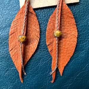 May include: A pair of brown leather feather earrings with gold chain accents and a brown stone bead on each earring.