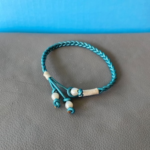 May include: A teal braided bracelet with three white pearl accents.