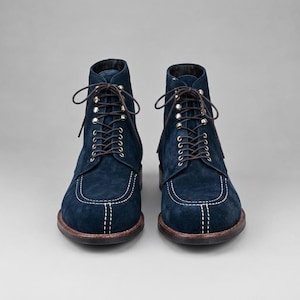 Botas artesanais de camurça azul-marinho com bico mocassim, sola de couro com costura contrastante e cadarço.