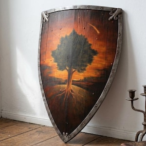 May include: A wooden heater shield featuring a painted scene of a large tree against an orange and brown sunset sky. The shield has a dark wood grain finish and is reinforced with a metallic silver border secured by evenly spaced metal rivets.