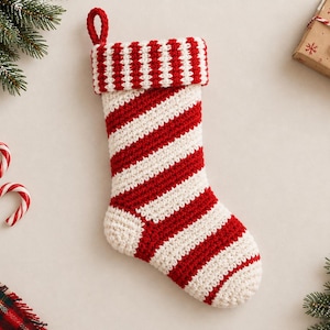 May include: A crocheted Christmas stocking featuring a diagonal red and white striped pattern throughout the body and a horizontal red and white striped cuff at the top. The stocking includes a small red crocheted loop for hanging purposes.