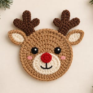 May include: A round, crocheted reindeer face coaster featuring a light brown head, dark brown antlers, cream-colored ears and muzzle, a bright red nose, black eyes, and small pink cheeks. The design includes a simple black stitched mouth.
