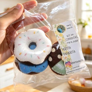 以下が含まれることがあります： 透明なビニール袋に入ったフェルト製のままごと用食品。白いアイシングとカラフルなスプリンクルが付いた茶色のドーナツ、青いドーナツ、白い水玉模様の茶色のドーナツが含まれています。ラベルには「MAPU WAWITA KIT de COMIDITAS PARA JUGAR HUERTA PANADERÍA @MAPUWAWITA」と記載されています。