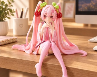 Puede incluir: Una figura de estilo anime con cabello rosa y largas coletas adornadas con accesorios de cerezas. El personaje viste un conjunto rosa claro con motivos de flores de cerezo, tiene ojos rojos y está sentado con las manos juntas cerca de la cara.